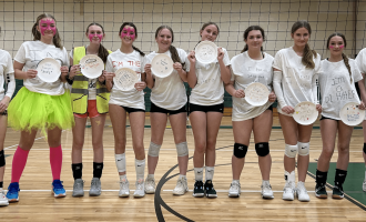 Girls volleyball team posing with paper plate awards indoors.